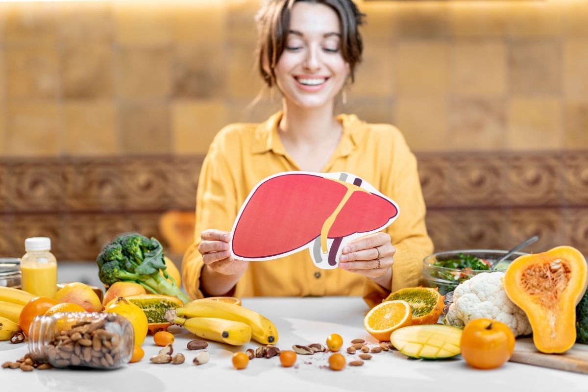 Woman holding an illustrated liver cutout surrounded by fresh produce for a liver reset